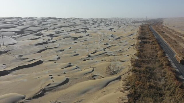 Aerial view of a straight highway cutting through the vast sand dunes of the Taklamakan Desert in Xinjiang, China.