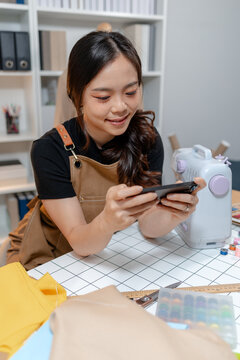 Professional fashion designer using a smartphone while managing a sewing studio and organizing tailoring supplies. Creative apparel production, small business and handmade craftsmanship.