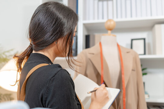 Fashion designer inspecting garment quality, measuring blazer fit and recording design details in a professional fashion studio. Apparel development, clothing quality control and textile craftsmanship