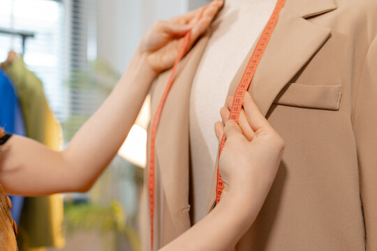 Fashion designer inspecting garment quality, measuring blazer fit and recording design details in a professional fashion studio. Apparel development, clothing quality control and textile craftsmanship