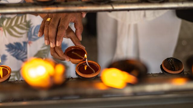A devotee lights a traditional clay oil lamp among rows of glowing lamps during a Buddhist religious ceremony