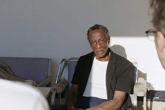 Senior Black man in a therapy session with a counselor, featuring dramatic lighting and a guarded expression for mental health and aging support