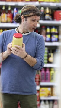 Man buyer examines display case, reads product label information before buy canned food. Client compares different options item, chooses product goods and check shelf life 