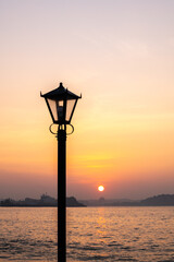 Obraz premium Sunset over the sea with a vintage street lamp silhouette