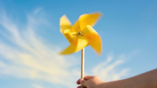 Yellow pinwheel spinning in hand against a bright blue sky with wispy clouds