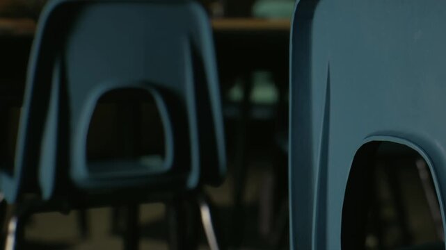 Several blue chairs are placed in a room with low lighting. The chairs are slightly out of focus, showcasing a quiet environment in a school or dining area.