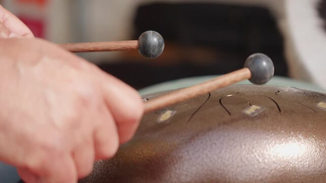 Close-up of hands playing a steel tongue drum with wooden mallets, creating a relaxing percussive performance with melodic and meditative tones.