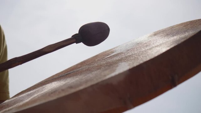 Low-angle close-up of a musician striking a traditional frame drum with a padded beater, capturing rhythmic movement during an acoustic percussion performance.