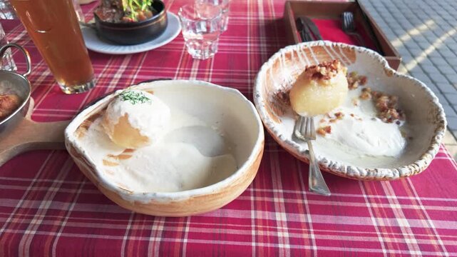 Delicious traditional dumplings served with creamy sauce and nuts on rustic dishes, set on a red plaid outdoor table with beer, salad, and daylight highlighting the vibrant scene.