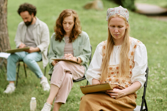 Diverse group of Caucasian young adults drawing on sketchbooks during outdoor art master class in park. Image suitable for promoting creative workshops and recreational education