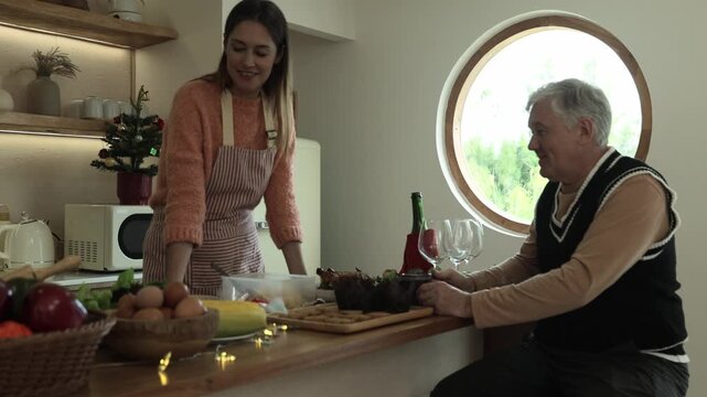 Father sat at the kitchen counter waiting for his daughter finish cooking and preparing food Christmas themed party preparing variety dishes including spaghetti and cookies.