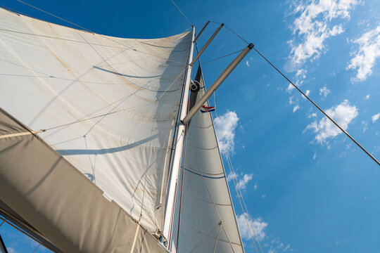 White sails filled with wind against a blue sky above a sailing yacht. Wind powered navigation and freedom at sea.