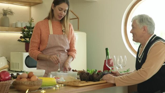 Father sat at the kitchen counter waiting for his daughter finish cooking and preparing food Christmas themed party preparing variety dishes including spaghetti and cookies.