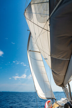 White sails filled with wind against a blue sky above a sailing yacht. Wind powered navigation and freedom at sea.