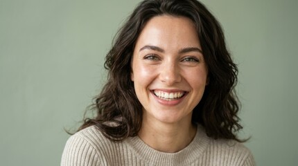 Fototapeta premium Beautiful young woman with dark curly hair smiling warmly in studio portrait against a soft green background representing wellness and happiness