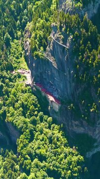 Vertical video. Altindere, Trabzon Province, Turkey. Sumela Monastery, a Greek Orthodox complex carved into a sheer cliff face, aerial drone view over dense coniferous forest and the winding Altinder