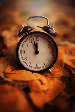 Black alarm clock on colorful maple leaves background. Closeup. Time change concept.