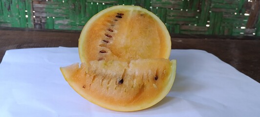 yellow watermelon or Citrullus lanatus cut open to show juicy golden flesh and dark seeds, with a front slice © Rustanto