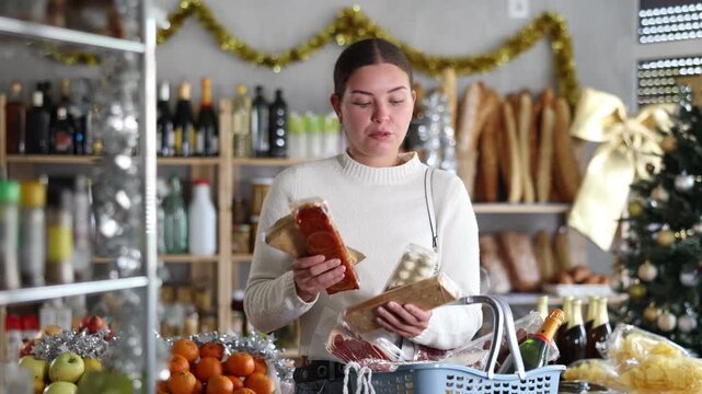 Cheerful young girl standing with shopping basket in grocery shop, surrounded by holiday decorations, holding packages of sweet nutty turron, choosing traditional Spanish desserts for Christmas feast