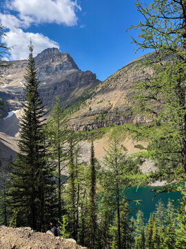 Hiker resting on Big Beehive trail above Lake Agnes with mountain peak, Banff