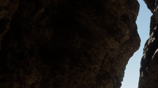 A narrow canyon allows light to pour in through tall rock formations. The sun shines brightly against the blue sky, casting shadows on the rugged surfaces.