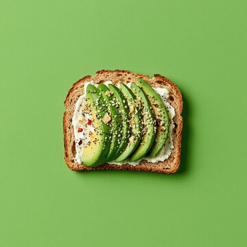 Fresh healthy vegetarian avocado toast with sliced avocado spread cream cheese and mixed seeds on whole grain bread placed on solid bright green background