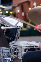 Fototapeta premium Musician performing on drums at an outdoor concert with dynamic hands, sticks and cymbals. Drummer hands striking cymbals and drums during a lively open-air summer music performance.