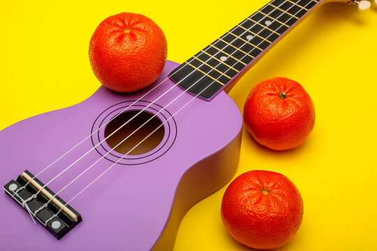 Fragment of a four-stringed ukulele guitar on a yellow background with tangerines