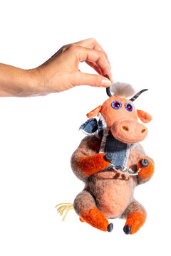A woman's hand holding a cow&mdash;a soft felt toy&mdash;on a white background.