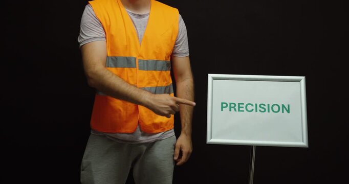 Worker in a safety vest pointing at a precision sign, representing accurate work, quality, manufacturing, engineering, and attention to detail.