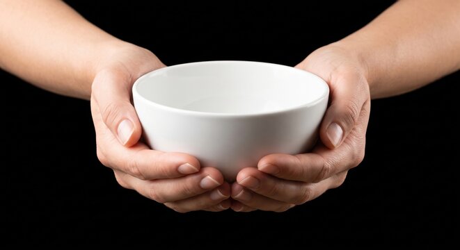 Hands holding empty white ceramic bowl against black background representing hunger poverty and need for food assistance or charity work.