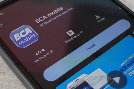 BCA mobile app page displayed on smartphone screen with finger touching install button, digital banking software download concept
