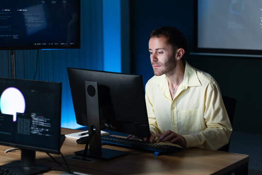 Concentration of Male Software Developer Looking at computer monitor, while working on software development, coding task, hand typing on keyboard writing code sit at desk in tech office night.