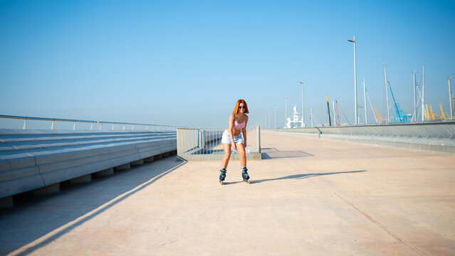 Young woman rollerblading along city port on sunny day