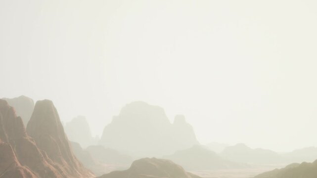 The scene shows mountains and hills in a desert area. Light mist covers the land. The early morning sun softly brightens the surroundings. The sky appears pale.