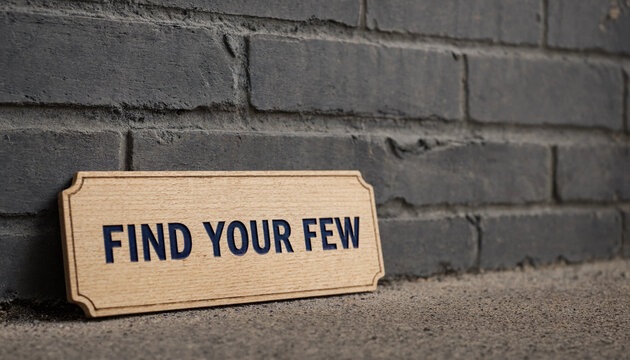 Wooden sign with text find your few leaning against gray brick wall concept for exclusivity or selective focus