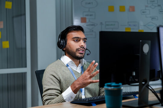 IT Help Desk Specialist Providing Online Technical Support, Explaining Computer Problem Solutions, troubleshooting software issues and assisting a customer through headset in office.