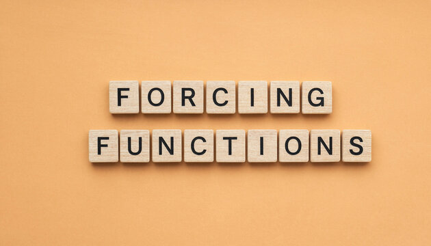 Forcing functions concept spelled out with wooden letter tiles on warm orange background