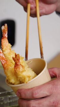 Chef Placing Crispy Shrimp Tempura into Paper Cup with Chopsticks
