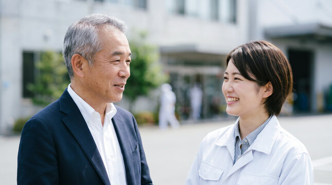 工場の敷地内で従業員と笑顔で会話する経営者