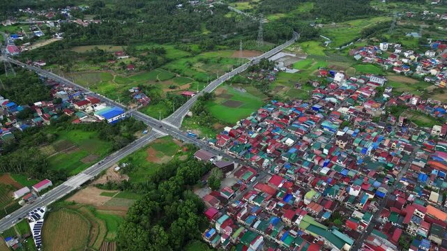 Smooth tracking drone footage following Lucban Bypass Road through rice fields and countryside neighborhoods with agricultural fields at Lucban, Quezon, Philippines during daytime.