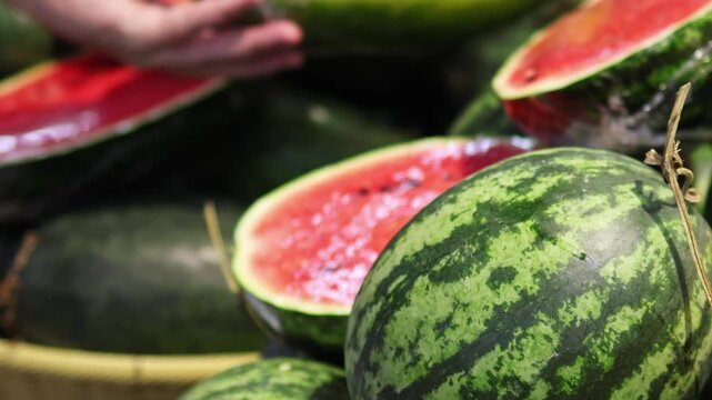 Close-up of watermelon with a shopper choosing a fruit before purchase in produce section in a blurry background. Concept of fresh food selection, grocery shopping, and everyday retail.