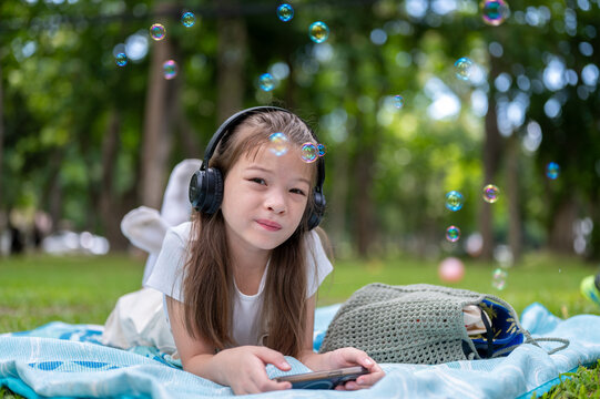 Young mixed race girl relaxing on a blanket while playing with a smartphone and bubbles in the park