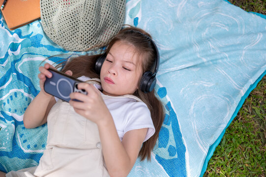 Young mixed race girl wearing headphones and looking at her smartphone while resting in the park
