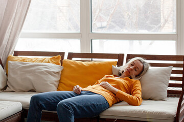 Middle aged woman lying on sofa at home holding stomach feeling unwell. Abdominal pain and chronic...