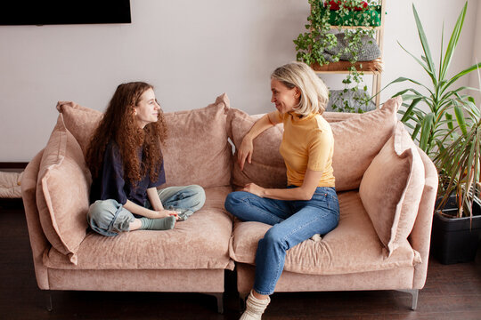 Woman talking with teenage daughter sitting on sofa at home. Mother and girl having conversation in living room. Family communication and parenting support concept.