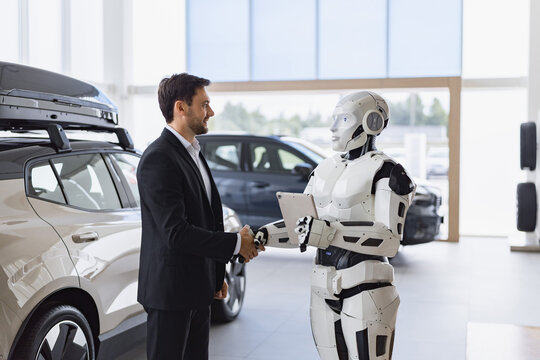 A human businessman and a humanoid robot shake hands in a modern car dealership, symbolizing future automotive sales