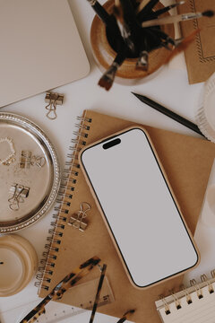 Top View Cozy Office Desk Layout Featuring Blank Phone Screen Mockup, Paintbrushes, And Pearl Jewelry