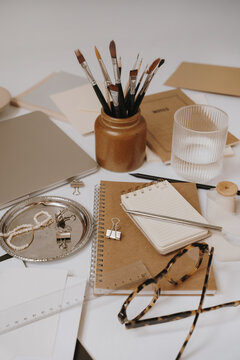 Aesthetic Earth Tone Home Office Workspace Arranged With Kraft Journals, Silver Pen, Glass Of Water, And Art Brushes