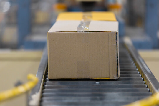 Cardboard box resting on moving conveyor belt inside busy factory. Efficient delivery and shipping process happening in modern warehouse environment ensuring steady package distribution